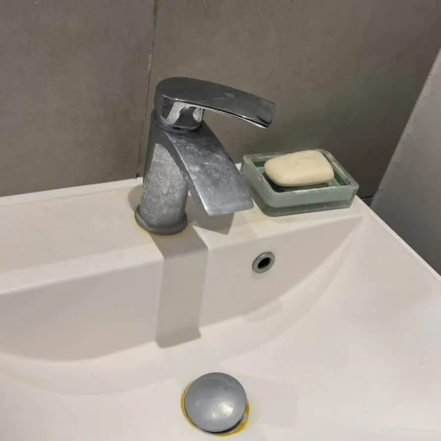 A bathroom basin with a tap dulled by limescale and a stained plug before cleaning