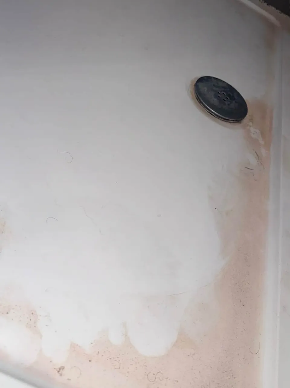 A shower tray with orange staining and soap scum before cleaning