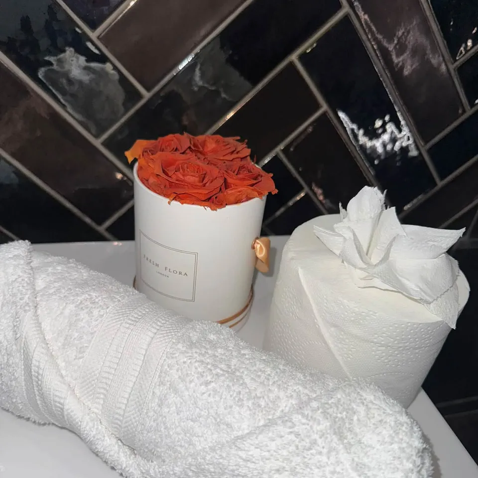 Rolled white towels and a vase of roses left neatly on a clean bathroom surface