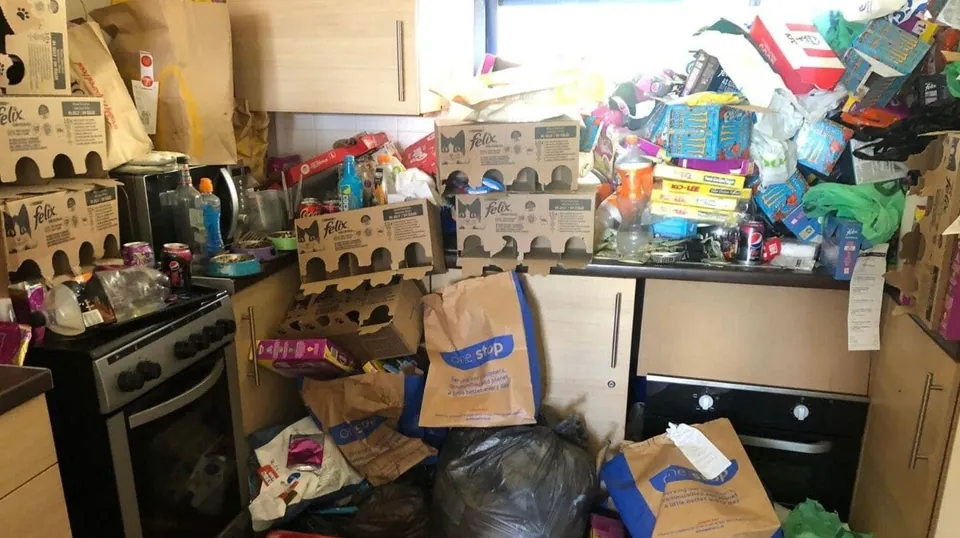 A cluttered kitchen in Ashford before cleaning, with worktops and floor covered in bags and boxes