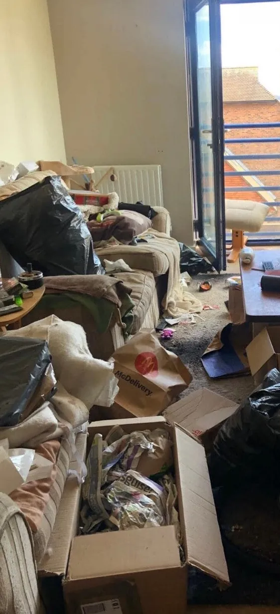 A living room before cleaning, covered in rubbish bags, boxes and clutter